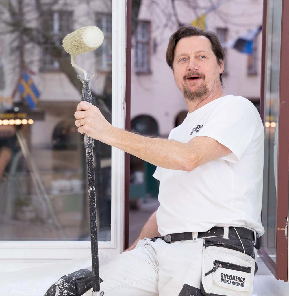 Mathias Svedberg från Svedbergs Måleri håller en färgroller i ett öppet fönster under ett målarjobb i Stockholm